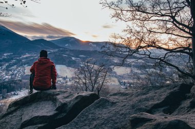 Gün batımında Ostravice yakınlarındaki Beskydy Dağları 'nda bir ayı kayasının üzerinde oturan kırmızı kahverengi ceketli genç bir çocuk. Geleceğini bir kayanın kenarında düşünürken.