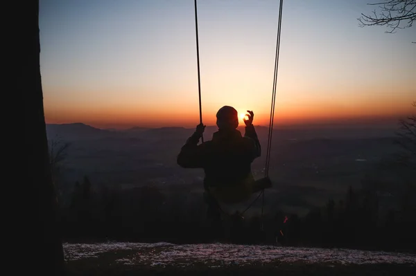 Hairy young boy aged 16-20 of European descent enjoys his life swinging on a swing at sunset on the top of Prasiva mountain in the Beskydy mountains in eastern Bohemia in Central Europe.