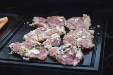 Adam dolu bir domuz boynunu fesleğen, tuz, biber ve yağla kurutmak için çelik bir kepçe kullanıyor. Açık havada ateşli bir ateşte barbekü. Barbekü sezonu başladı..