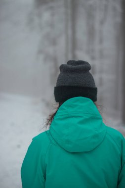 Yeşil kışlık ceketli genç kız Avrupa 'daki Beskydy dağlarında çirkin, sisli ve soğuk havada yürüyor..