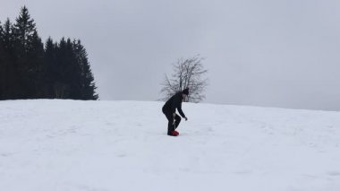 Man from the village in black winter clothes rides down the slope on a plastic snowboard. Falling on his ass. Crashing in the snow. Winter fun. Full HD