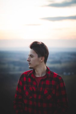 20 'li yaşlarda, siyah ve kırmızı tişörtlü bir adamın samimi portresi. Geleceğine bakıyor, düşüncelerine dalmış ve derin derin düşünüyor. Kararsız bir yolculuktaki genç bir adamın otantik ruh hali..