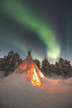 Sami 'nin Norveç' in vahşi doğasında Lavvu inşa ettiği büyülü Noel atmosferi, kuzey ışıklarının patlaması gökyüzünü dolduruyor. Sıcak atmosfer. Kuzey Norveç, Tromso Bölgesi