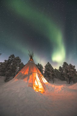 Sami 'nin Norveç' in vahşi doğasında Lavvu inşa ettiği büyülü Noel atmosferi, kuzey ışıklarının patlaması gökyüzünü dolduruyor. Sıcak atmosfer. Kuzey Norveç, Tromso Bölgesi