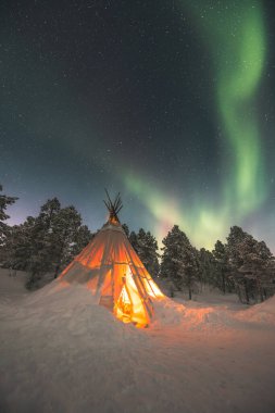 Sami 'nin Norveç' in vahşi doğasında Lavvu inşa ettiği büyülü Noel atmosferi, kuzey ışıklarının patlaması gökyüzünü dolduruyor. Sıcak atmosfer. Kuzey Norveç, Tromso Bölgesi