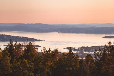 Adaları, sakin suları ve ormanlık tepeleriyle Oslofjord 'un üzerinde yumuşak pastel günbatımı yumuşak İskandinav akşam havasını ve altın huzurunu yansıtıyor..
