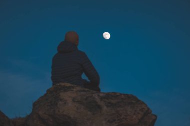 Norveç 'te açık gece gökyüzünde Ay' ın altındaki kayalıklarda yalnız gezgin oturuyor. Yalnızlığın, düşüncenin ve doğadaki minimalizmin şiirsel anı