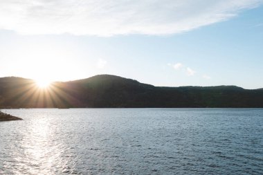 Norveç 'in Setesdal Vadisi' ndeki sakin gölün üzerindeki altın ışık. Yumuşak tepeler ve durgun sular sıcak günbatımı tonlarını yansıtarak Norveç 'in vahşi doğasının barışçıl özünü yakalıyor.