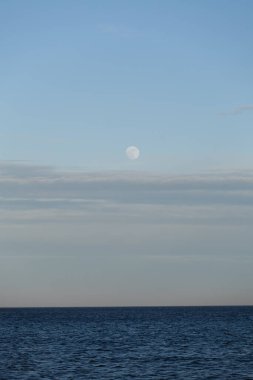 Danimarka, Skagen yakınlarındaki Kuzey Denizi 'nin sakin sularında dolunay yükseliyor. Minimalist İskandinav deniz manzarası yumuşak mavi ışıkla yıkandı.