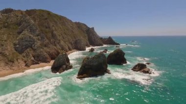 Lizbon, Portekiz yakınlarında yüksek drone manzaralı bir sahil. Kuma çizilmiş araç izleri yumuşak Atlantik dalgalarıyla karşılaşıyor. Hava görüntüleri karayla deniz arasındaki doğal desenleri ve kontrastı gösteriyor..