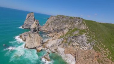 Lizbon, Portekiz yakınlarında yüksek drone manzaralı bir sahil. Kuma çizilmiş araç izleri yumuşak Atlantik dalgalarıyla karşılaşıyor. Hava görüntüleri karayla deniz arasındaki doğal desenleri ve kontrastı gösteriyor..