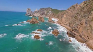 Lizbon, Portekiz yakınlarında yüksek drone manzaralı bir sahil. Kuma çizilmiş araç izleri yumuşak Atlantik dalgalarıyla karşılaşıyor. Hava görüntüleri karayla deniz arasındaki doğal desenleri ve kontrastı gösteriyor..