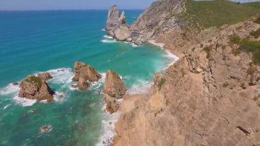 Lizbon, Portekiz yakınlarında yüksek drone manzaralı bir sahil. Kuma çizilmiş araç izleri yumuşak Atlantik dalgalarıyla karşılaşıyor. Hava görüntüleri karayla deniz arasındaki doğal desenleri ve kontrastı gösteriyor..