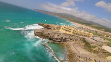 Lizbon, Portekiz yakınlarında yüksek drone manzaralı bir sahil. Kuma çizilmiş araç izleri yumuşak Atlantik dalgalarıyla karşılaşıyor. Hava görüntüleri karayla deniz arasındaki doğal desenleri ve kontrastı gösteriyor..