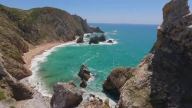 Lizbon, Portekiz yakınlarında yüksek drone manzaralı bir sahil. Kuma çizilmiş araç izleri yumuşak Atlantik dalgalarıyla karşılaşıyor. Hava görüntüleri karayla deniz arasındaki doğal desenleri ve kontrastı gösteriyor..