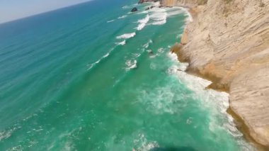 Lizbon, Portekiz yakınlarında yüksek drone manzaralı bir sahil. Kuma çizilmiş araç izleri yumuşak Atlantik dalgalarıyla karşılaşıyor. Hava görüntüleri karayla deniz arasındaki doğal desenleri ve kontrastı gösteriyor..