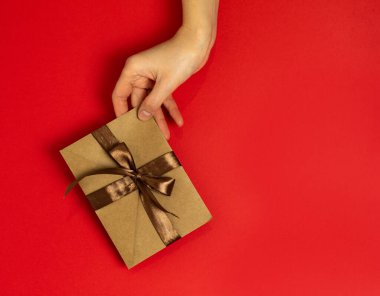 Kırmızı arka planda kurdele olan hediye zarfını tutan bir el.