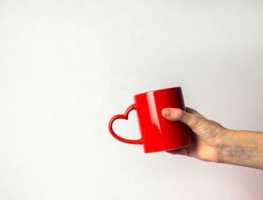 Kalp şeklinde saplı kırmızı bardağı tutan bir el.