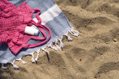 Plaj havlusunda pembe bir ağ torbasından süzülen SPF kremini gösteren düz bir taban..