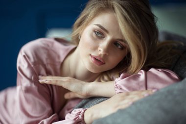 Yakından çekilmiş genç sarışın kadın portresi. Dalgalı saçlı, pembe pijamayla dalgalanıyordu. Metin uzayı