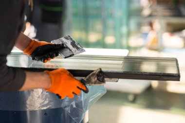 Seçici odaklanma, plastik pencere üretimi. Erkek, turuncu koruyucu eldivenler ve bir spatulayla cam eklem yerine özel bir çözüm uygular. .