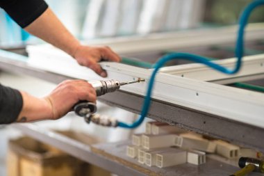 Seçici odaklanma, plastik pencere üretimi. Kendini tıklatan bir vidayı plastik bir pencerenin çerçevesine monte eden erkek bir işçinin yakın plan fotoğrafı. .