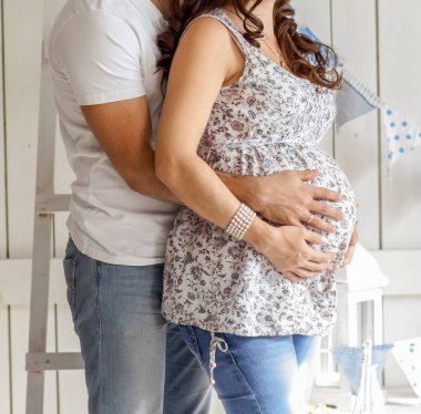 Aile fertlerinin tazelenmesini bekleyen genç evli bir çift. Kocası hamile karısının karnına sarılıyor..