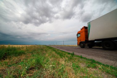 Gökgürültüsü bulutlarının asılı olduğu tarlalar arasında bir asfalt yol.