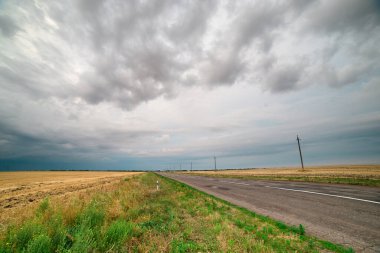 Gökgürültüsü bulutlarının asılı olduğu tarlalar arasında bir asfalt yol.