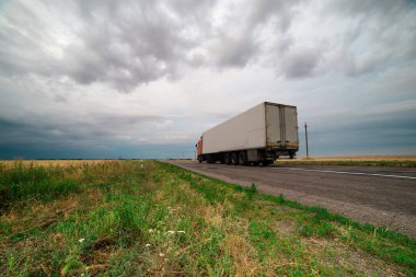 Gökgürültüsü bulutlarının asılı olduğu tarlalar arasında bir asfalt yol.
