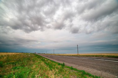 Gökgürültüsü bulutlarının asılı olduğu tarlalar arasında bir asfalt yol.