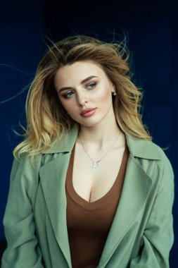 Masummuş gibi görünen çok seksi bir sarışın mavi bir duvarın arkasında kameraya poz veriyor. Vantilatör çerçevesindeki dağınık saçlar modelin güzel yüzü .