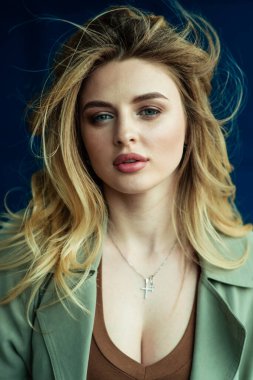 Masummuş gibi görünen çok seksi bir sarışın mavi bir duvarın arkasında kameraya poz veriyor. Vantilatör çerçevesindeki dağınık saçlar modelin güzel yüzü .