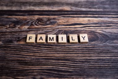 Kahverengi ahşap arka planda harfleri olan alfabe bloklarının üst görüntüsü. Yazıt AilesiComment.