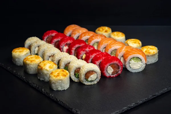 Japanese food, set of baked rolls, rolls in white sesame, red tobiko caviar, Philadelphia with curd cheese on a black slate board.