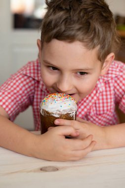 Odak fotoğrafı dışında. Paskalya pastası, beyaz ahşap bir masanın arka planındaki bir çocuğun ellerinde..