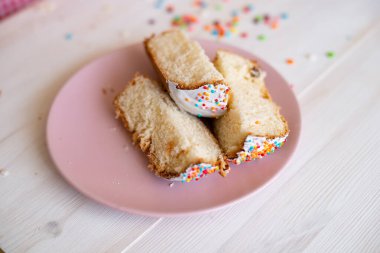 Paskalya pastası dilimleri pembe bir tabakta beyaz tahta bir masa arkasında.
