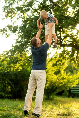 Mutlu baba mutlu bir şekilde oğlunu bahçeye fırlatıyor. Babalar Günü. Aile mutluluğu, babalık, açık hava oyunları..