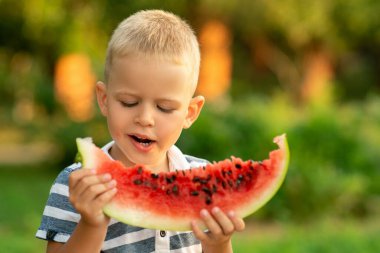 Çocuk dışarıda karpuz yiyor. Kırsalda yaz tatili.