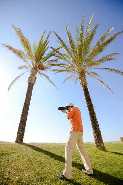 Fotógrafo turista em grama verde, palma e fundo céu azul — Fotografia de Stock