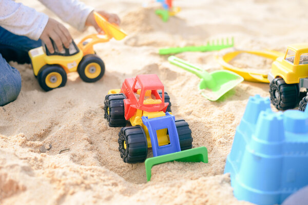 Ребенок веселится на улице. Ребёнок играет со своими игрушками на грузовике в солнечный летний день на фоне песка
 .