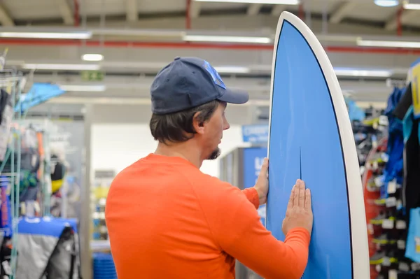 Back view of male surfer holding a surf board on shop background