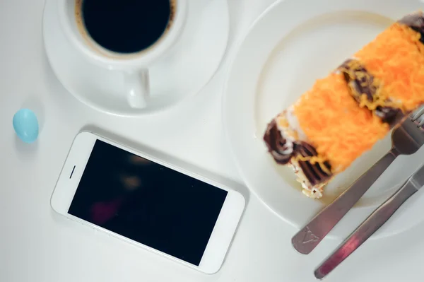 Primo piano vista dall'alto di tazza di caffè, smartphone e torte sullo sfondo del tavolo. Posa piatta — Foto Stock