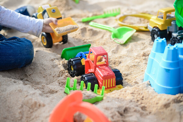 Ребенок веселится на улице. Ребёнок играет со своими игрушками на грузовике в солнечный летний день на фоне песка
 .