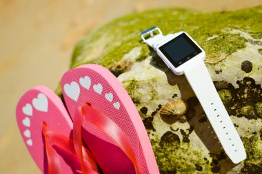 Closeup akıllı izlemek ve plaj arka plan üzerinde parmak arası terlik. Ana sayfa görünümü stili, fotoğraf ve video dışında