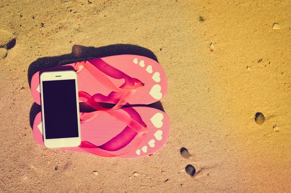 Primer plano en el teléfono inteligente y chanclas en el fondo de la playa. Estilo de vista superior, foto y video exterior — Foto de Stock