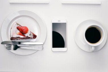 Closeup düz kahve fincanı, akıllı telefon ve kek ahşap zemin üzerinde yatıyordu. Üstten Görünüm