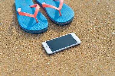 Üstten Görünüm yakın çekim yaz plaj arka plan üzerinde cep telefonu flip flop üzerinde. Mutlu neşeli tatil