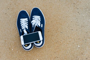 Kumlu yaz plaj arka plan üzerinde ayakkabı ile üstten görünüm üstünde hareket eden telefon. Yakın, mutlu neşeli tatil