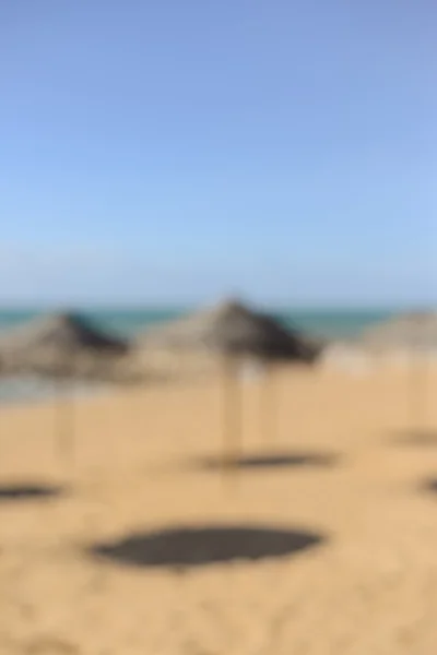 Playa exótica con sombrillas de palmeras, arena dorada. Siluetas desenfocadas —  Fotos de Stock